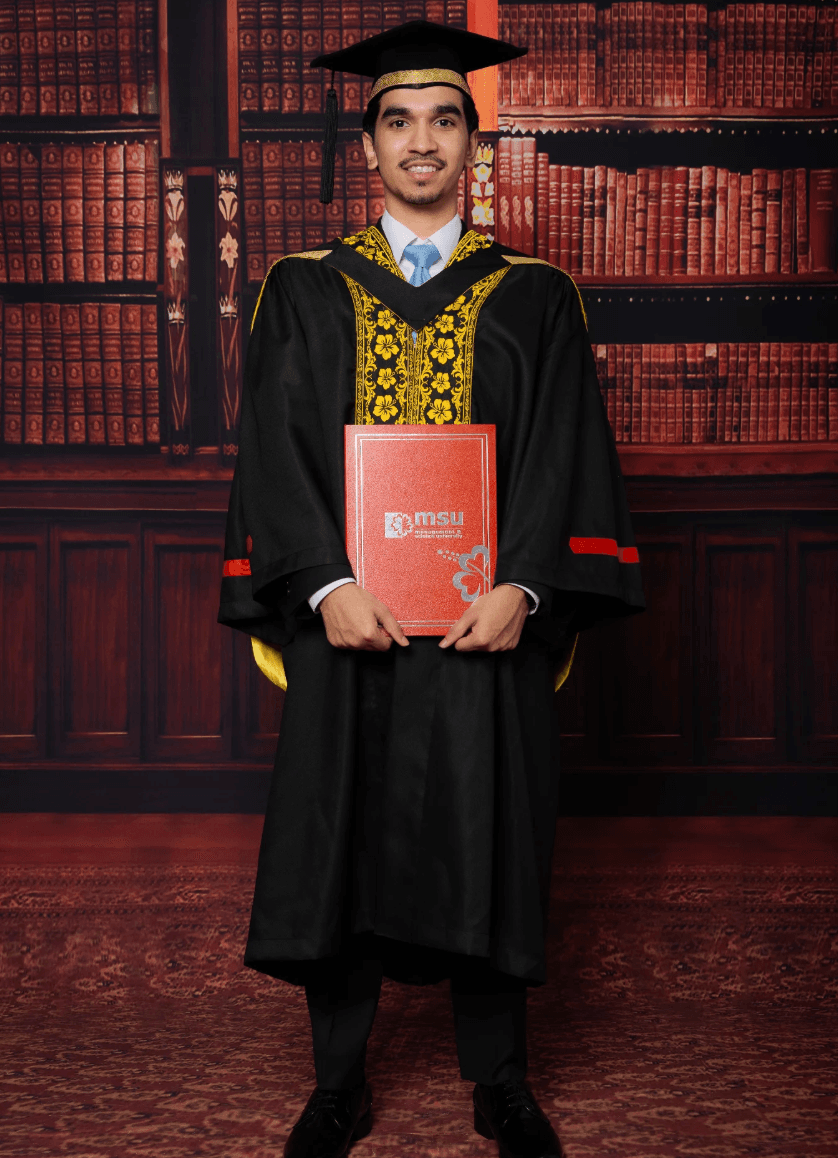 Graduan berjubah hitam bertepi emas pegang skrol merah